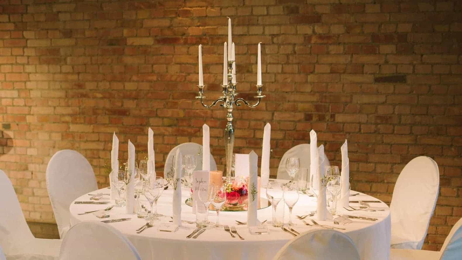 Hochzeitstisch mit hohem Kerzenleuchter vor einer Backsteinwand