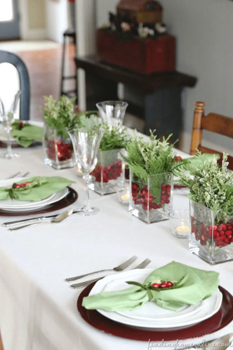 Lange weiße Festtafel mit grünen Zweigen, roten Gläsern und Kerzen