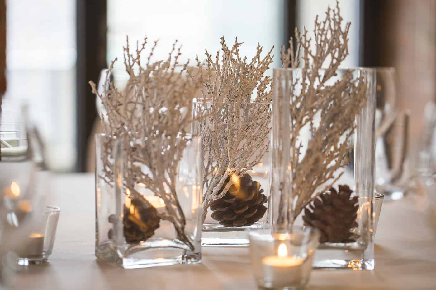Winterliche Zweige in hohen Glasvasen mit Tannenzapfen auf einem gedeckten Tisch