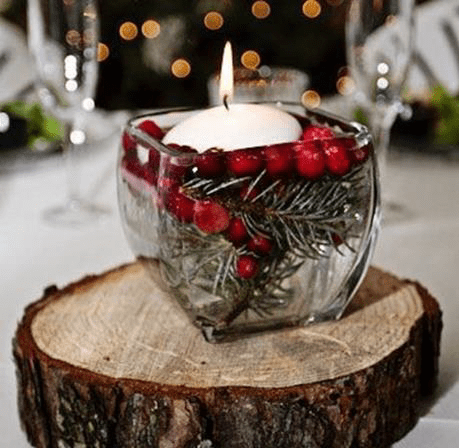 Schwimmkerze und rote Beeren in einem Glas auf einer Holzscheibe