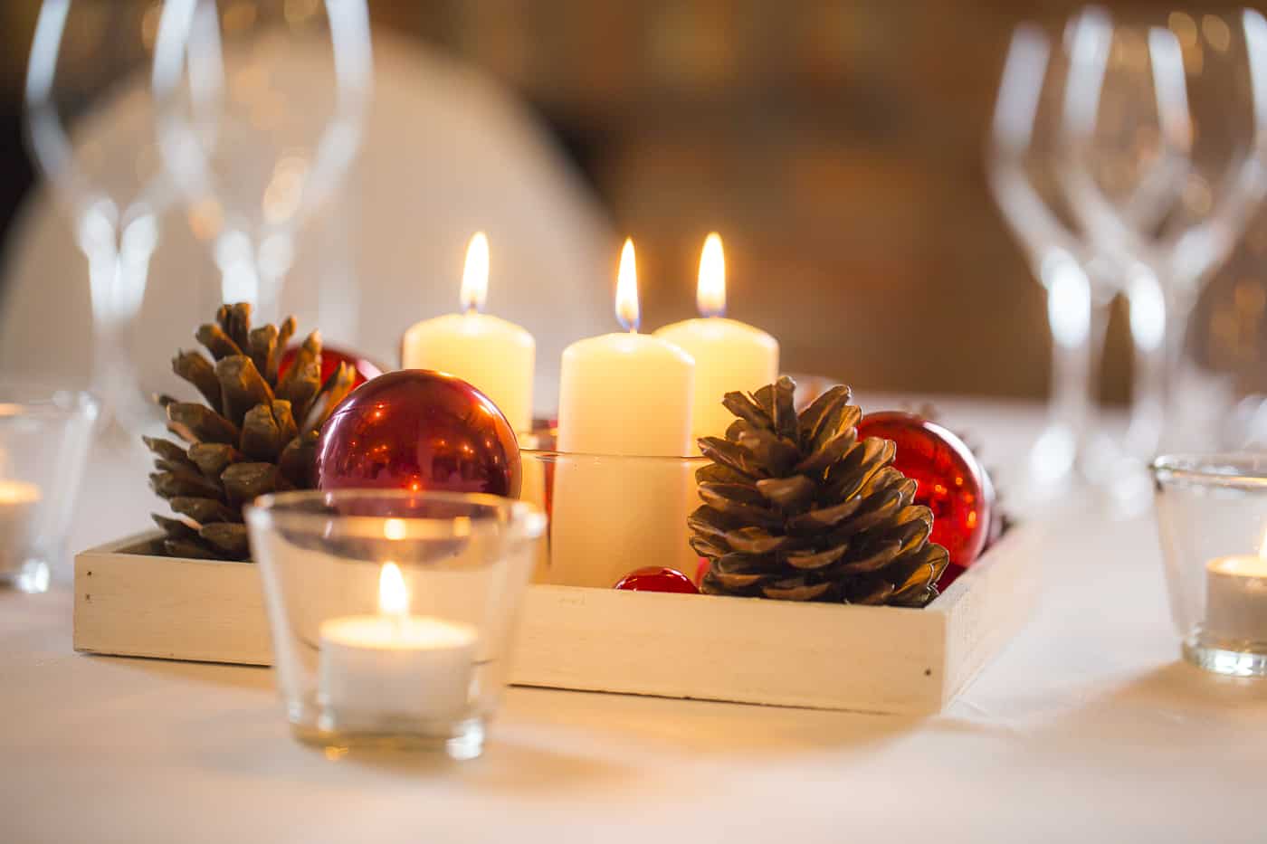Weiße Kerzen, Tannenzapfen und eine rote Weihnachtskugel auf hellem Teller
