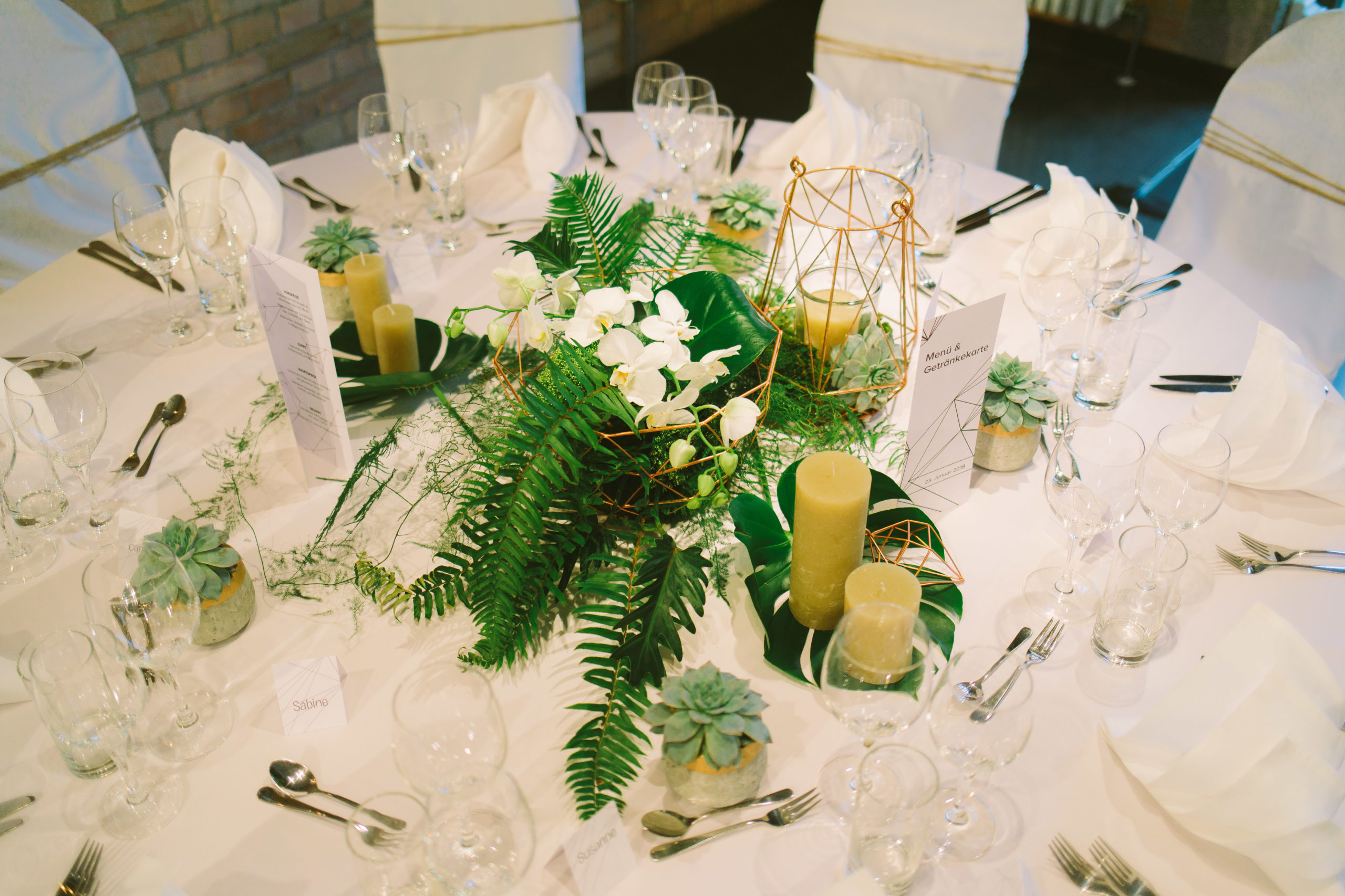 Modernes Tischarrangement mit weißen Blüten, Grün und geometrischem Glasgefäß