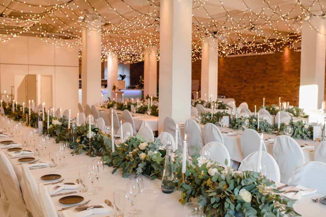 Lange Hochzeitstafel unter Lichterketten im Backsteinloft