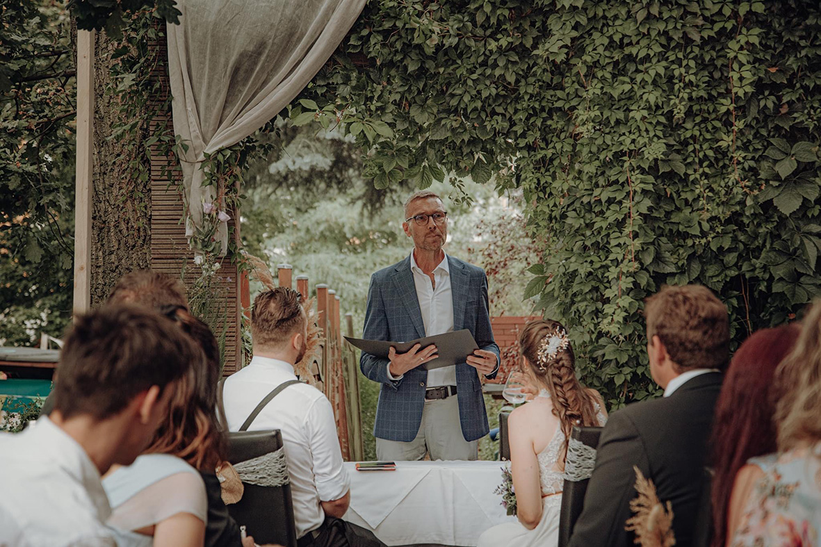 Impression von Eric Pullen: eine Hochzeitsgesellschaft verfolgt eine freie Trauung im Garten
