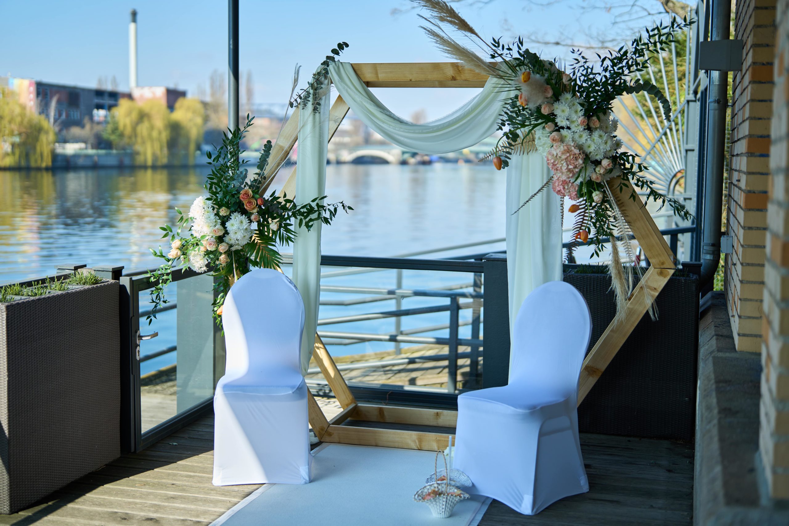 Trautisch mit Blumenschmuck und weißen Stühlen unter dem Traubogen