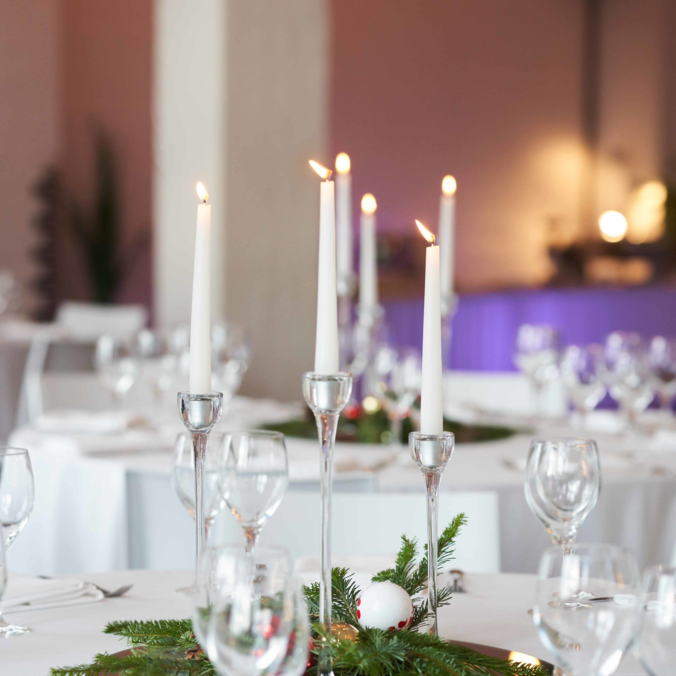 Drei schlanke Glaskerzenleuchter mit weißen Kerzen auf einer festlichen Tafel